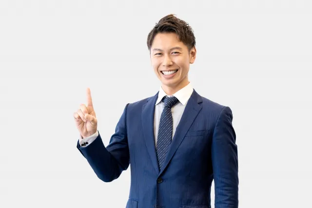 右の人差し指を上げているスーツを着た笑顔の男性
